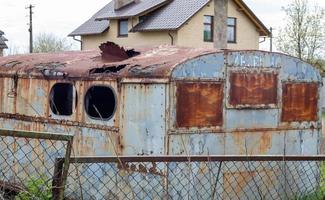 Eine heruntergekommene, verrottete und rostige Metallhütte auf einer Baustelle. ein alter Blechbauwagen mit rundem Dach und kaputter Scheibe von einer Wiese oder Weide mit Anhängerdeichsel. foto