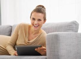 glückliche junge Frau, die auf Sofa mit Tablette PC liegt foto