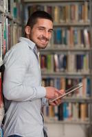 glücklicher männlicher Student, der mit Laptop in Bibliothek arbeitet foto
