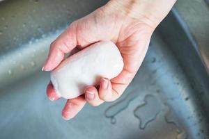 Frau hält Seife in der Hand über dem Waschbecken. konzept zur behandlung der haut der hände vor viren und mikroben. foto