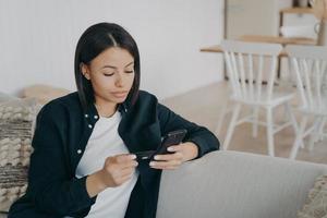 Online-Banking. weibliche mieter halten kreditkarte zahlen miete per handy-app auf der couch sitzend foto