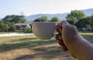 eine Hand, die eine Tasse Kaffee aus weißer Keramik mit natürlichem Hintergrund hält. erfrischungsgetränke für ein gutes morgenkonzept foto