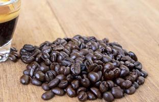 Geschlossener Haufen braun gerösteter Bio-Kaffeebohnen auf einem rustikalen Holztisch in der Nähe einer Tasse Espresso. Selektiver Fokus mitten in einem Kaffeehaufen foto