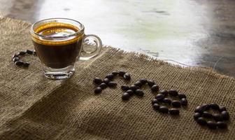 Hochwinkelansicht einer Tasse schwarzen Espressokaffees mit einer schönen Crema auf Sackleinen und brauner Arabica-Kaffeebohne. natürliches Sonnenlicht. erfrischen sie sich mit einem heißen getränk in einem morgenkonzept foto