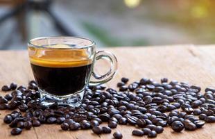 Bild einer Tasse heißen Espressokaffees mit einer schönen Crema auf einem Holztisch mit gerösteten braunen Bio-Kaffeebohnen im natürlichen Hintergrund mit orangefarbenem Sonnenlicht. Konzentrieren Sie sich auf eine Tasse Kaffee foto