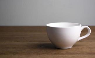 Vorderansicht der weißen Kaffeetasse aus Keramik auf einem braunen rustikalen Holztisch. foto