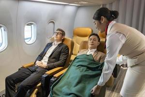 Flugbegleiter steckt die Decke für den schlafenden Passagier für Bordservice, Flugreisen und Transportkonzept ein foto
