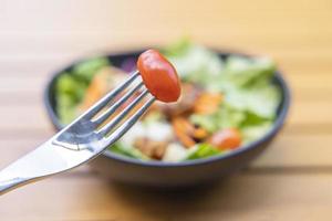 Verwenden Sie eine Gabel, einen Tomatenspieß im Vordergrund und einen Salat im Hintergrund. Frühstückssalat mit sautiertem Gemüse auf einem Holztisch foto