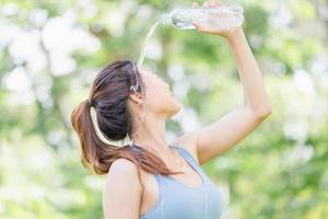 Sportlerin junge schöne Frau trinkt und spritzt Wasser in ihr Gesicht im grünen Sommerpark, Sportlerin trinkt Wasser aus einer Plastikflasche nach dem Training foto