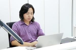 asiatischer langhaarkerl fokussiert und konzentriert sich auf seine arbeit vor dem laptop im büro. foto