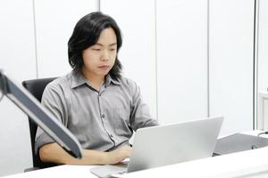 asiatischer langhaarkerl fokussiert und konzentriert sich auf seine arbeit vor dem laptop im büro. foto