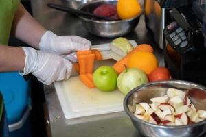 Die Hand der Frau schneidet das Karottengemüse und Obst wie Apfel-Guava-Orange auf der Plastikplatte in der dunklen Umgebungsküche. foto