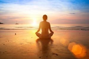 Frau, die Yoga am Strand bei Sonnenuntergang praktiziert.