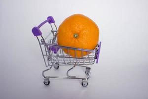 mini dekorativer Einkaufswagen mit großer orangefarbener Mandarine auf weißem Hintergrund. foto