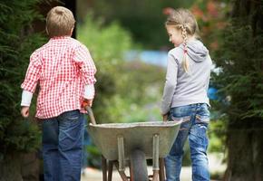 zwei Kinder spielen mit Schubkarre im Garten foto