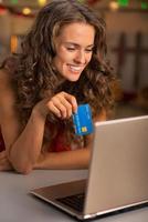 Porträt der glücklichen jungen Frau mit Kreditkarte unter Verwendung des Laptops foto