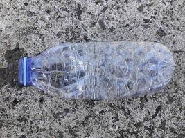 eine Plastikflasche mit Trinkwasser, die auf dem Straßenboden verstreut ist foto