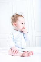 süßes Baby, das am Finger in einem weißen Kinderzimmer saugt foto