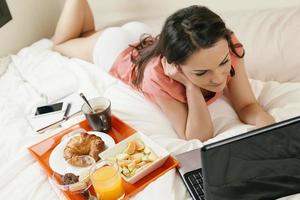Frau beobachtet den Laptop und frühstückt foto