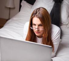 junge Frau, die Laptop auf ihrem Bett betrachtet foto