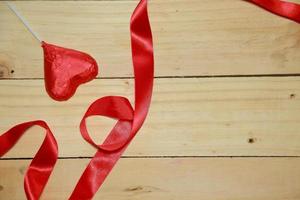 entwerfen Sie rotes herzförmiges Band und Schokoladenherz auf altem gealtertem hölzernem Hintergrund. Valentinstag-Konzept. Platz für Text. foto