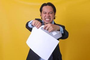 emotionaler junger Geschäftsmann, der Papier auf gelbem Hintergrund zerreißt foto