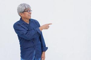 Asiatischer Senior im Denim-Casual-Stil zeigt mit dem Zeigefinger isoliert auf weißem Hintergrund mit Kopierraum. foto