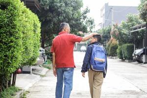 Rückseite des Großvaters, der den Kopf des Enkels streichelt, während er zur Schule geht. konzept für eltern- und familienaktivitäten. foto