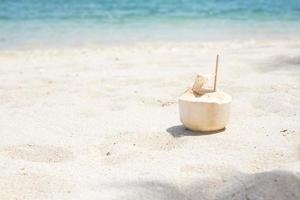 Frischer Kokosnusssaft und Stroh auf weißem Sand vor tropischem Strandhintergrund. sommer-, entspannungs- und urlaubskonzepte foto