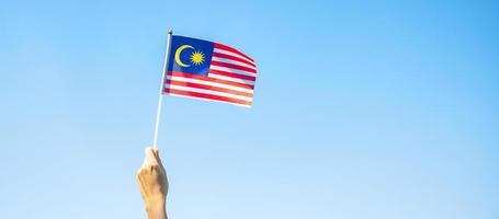 Hand, die Malaysia-Flagge auf Hintergrund des blauen Himmels hält. september malaysischer nationaltag und august unabhängigkeitstag foto