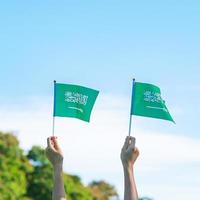Hand, die Saudi-Arabien-Flagge auf Hintergrund des blauen Himmels hält. september saudi-arabien nationalfeiertag und fröhliche feierkonzepte foto