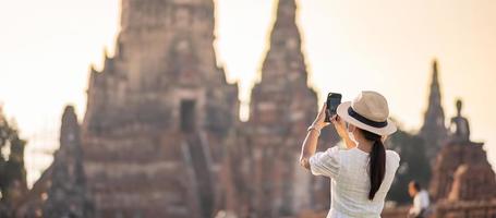 glückliche touristische frau, die chirurgische gesichtsmaske trägt und foto mit mobilem smartphone macht, schutz covid-19-pandemie während des besuchs im ayutthaya-tempel. neues Normal-, Sicherheitsreise- und Reisekonzept