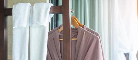 Nahaufnahme sauberer Bademantel und Handtuch, die im Holzschrank im Luxushotel hängen. Entspannungs- und Reisekonzept foto