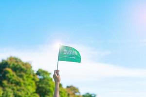 Hand, die Saudi-Arabien-Flagge auf Hintergrund des blauen Himmels hält. september saudi-arabien nationalfeiertag und fröhliche feierkonzepte foto
