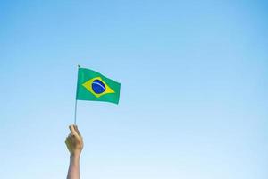 Hand, die Brasilien-Flagge auf Hintergrund des blauen Himmels hält. september unabhängigkeitstag und fröhliche feierkonzepte foto