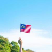Hand, die Malaysia-Flagge auf Hintergrund des blauen Himmels hält. september malaysischer nationaltag und august unabhängigkeitstag foto