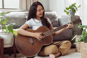 Frau, die zu Hause Gitarre spielt. schöne Frau lächelt und spielt Gitarre mit ihren Pflanzen im Wohnzimmer. foto