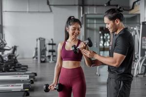 asiatische frau trainiert mit persönlichem trainer im fitnessstudio. asiatische gesunde frau, die armtraining in fitnees mit persönlichem trainer macht. foto