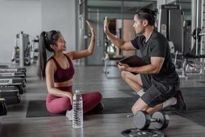 asiatische Frauenübung mit persönlichem Trainer im Fitnessstudio. gesunde frau gib mir fünf mit personal trainer. foto