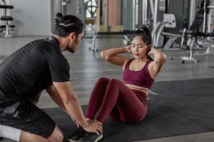 asiatische Frauenübung mit persönlichem Trainer im Fitnessstudio. gesunde frau, die abs-training in der fitness mit persönlichem trainer macht. foto