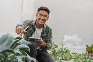 asiatischer Bauer im Gemüse-Bio-Bauernhof. männliche gärtner verwenden tabletten, um die wachstumsqualität von gemüse auf dem bauernhof zu überwachen. Hydroponisches Bio-Bauernhof-Konzept. foto