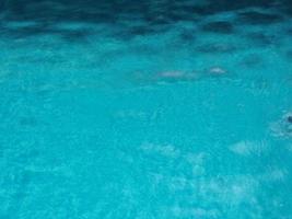 Regentropfen, die blaues Wasser im Poolhintergrund fallen lassen, kräuseln sich auf der Oberflächenstruktur, glitzernde Bokeh-Zusammenfassung foto