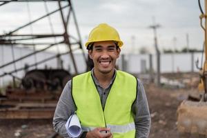 ingenieurmann, der auf der baustelle arbeitet. asiatischer arbeitermann, der auf der baustelle lächelt und die arme verschränkt. foto