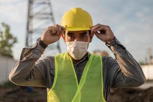 ingenieurmann, der gesichtsmaske trägt und auf der baustelle arbeitet. junger arbeiter, der auf der baustelle arbeitet. foto