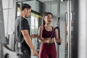 asiatische Frauenübung mit persönlichem Trainer im Fitnessstudio. junge gesunde Frau trainiert in Fitness mit persönlichem Trainer. foto