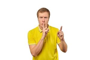 lustiger Mann im gelben T-Shirt, der darum bittet, ruhig zu sein, Schweigegeste, weißer Hintergrund foto