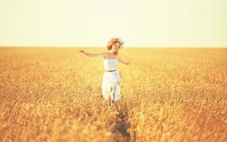 glückliche junge Frau, die das Leben im goldenen Weizenfeld genießt foto