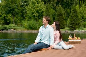 glückliches romantisches Paar, das Picknick in einem Park nahe See genießt