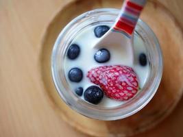 Draufsicht Nahaufnahme lebendige Farbe frischer kalter Milch mit frischen Früchten Erdbeeren und Heidelbeeren mit weiß-rotem Streifenlöffel foto