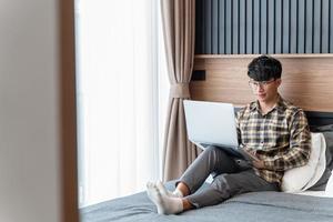 Ein männlicher Freiberufler verbringt Zeit damit, friedlich auf seinem Bett mit seinen Laptops zu arbeiten foto